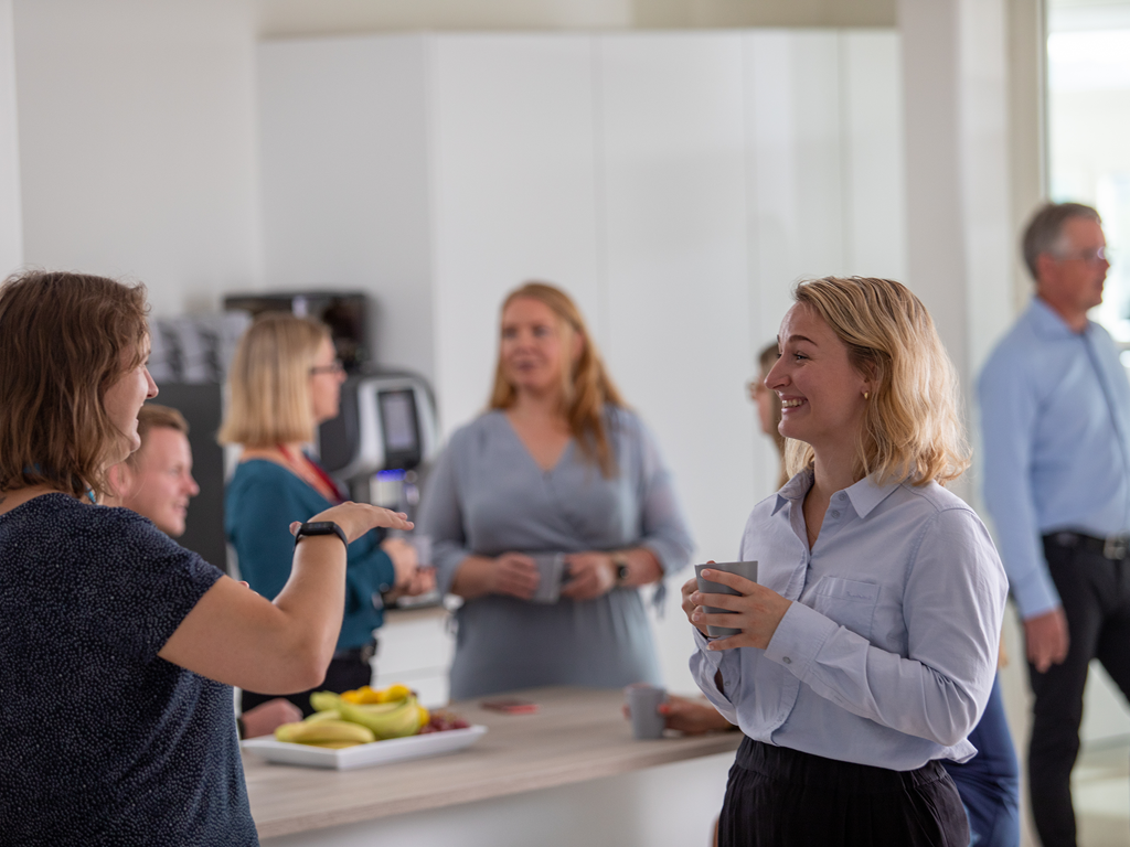 Två kvinnor i fokus i lunchrummet, den ena berättar något och den andra skrattar
