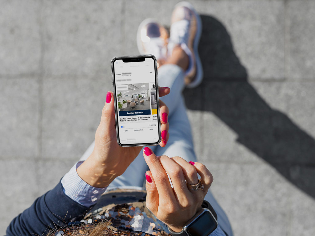 Kvinna som tittar på sin mobil, sittandes på en solig trottoar