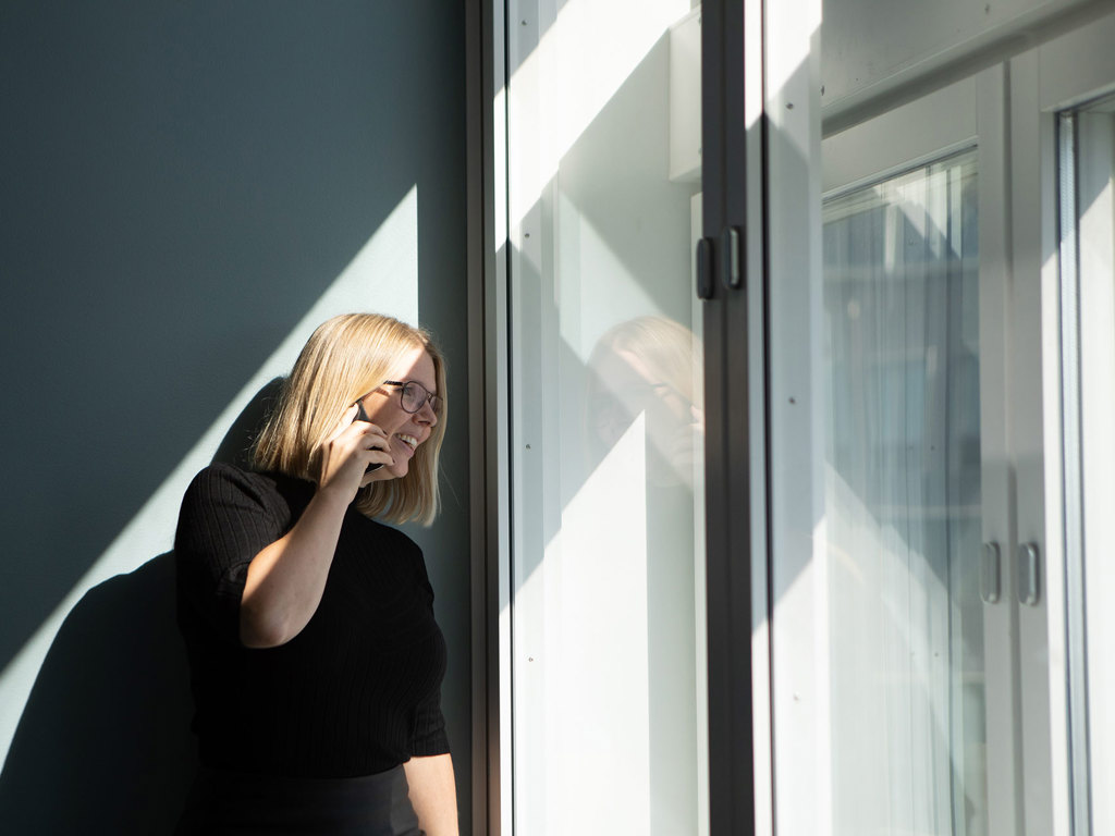 Kvinna håller och pratar i mobil och ser ut genom fönster